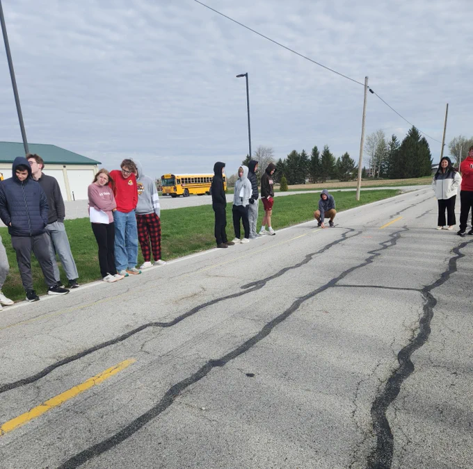 A student measures a "crash scene." Students are taught crash reconstruction. They are standing on or alongside a road.