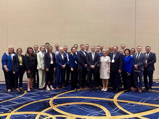 Delegation standing on blue and gold carpet with Assistant Secretary Fogel.