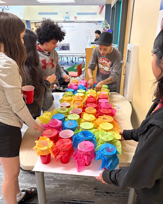 Several students working on a colorful art project using cups and paper plates in a classroom setting.