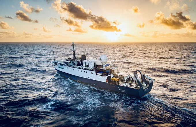 Exploration Vessel Nautilus sails across a choppy blue ocean under a bright, golden sunset with scattered clouds.