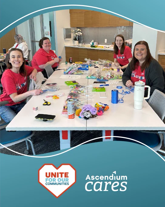 A group of people are sitting around a table covered with various craft supplies and snacks. There are logos for "Unite for our Communities" and "Ascendium Cares" at the bottom of the image.