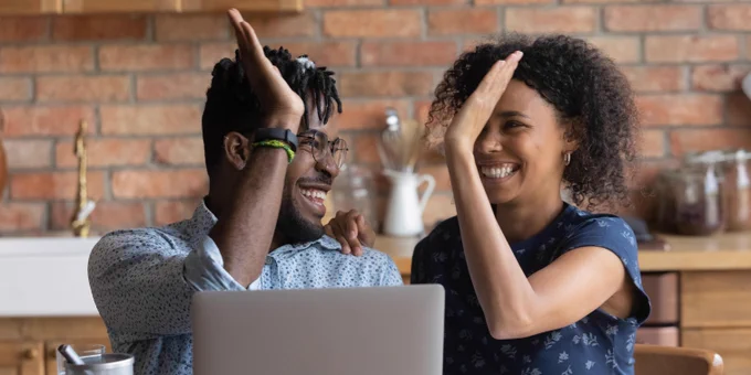 Couple high fiving while seated at a table in front of an open laptop.