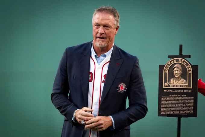 Mike Timlin stands next to his Red Sox Hall of Fame plaque ooking out at Fenway Park from the infield while wearing Red Sox Hall of Fame suit coat.
