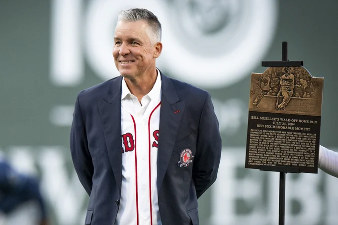 Bill Mueller smiles and stands next to his Red Sox Hall of Fame Memorable Moment plaque looking out at Fenway Park from the infield while wearing Red Sox Hall of Fame suit coat over a Red Sox home white jersey. 
