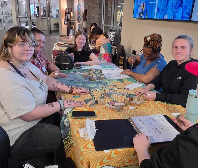 A group of people are gathered around a table covered with a colorful cloth, engaged in an activity.