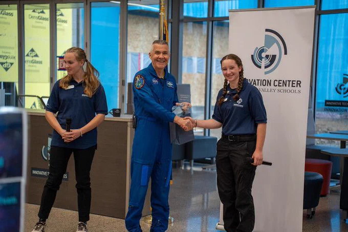 Two students pose for a photo with a former astronaut.