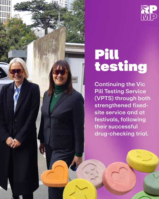 Two people smiling and wearing sunglasses stand outside, beside a promotional banner for the Vic Pill Testing Service. The banner highlights drug-checking trial successes and expansion plans.