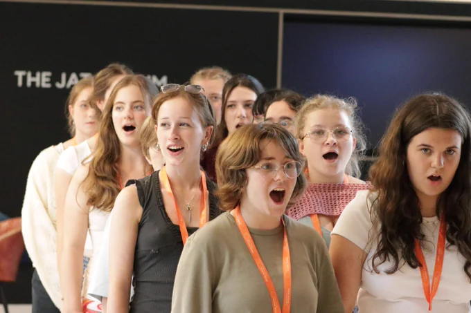Group of young adults standing in a line indoors, each wearing an orange lanyard around their necks.