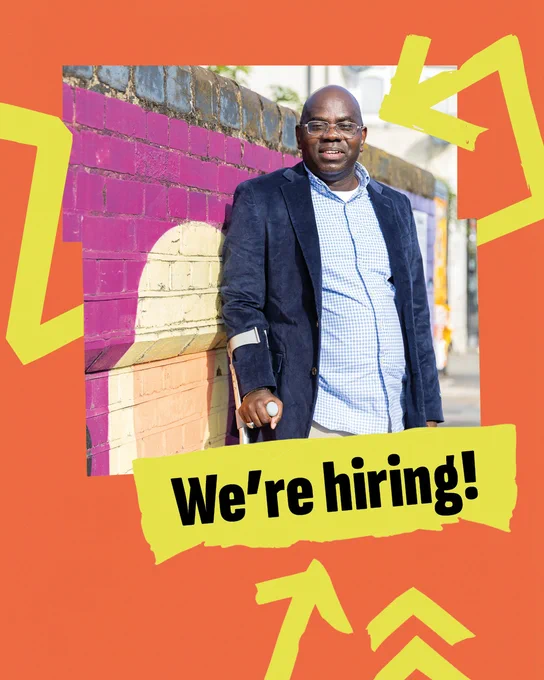 An image of a disabled person standing in front of a colourful mural, smiling at the camera. The image is in a jagged frame on a bright orange background. Bright yellow arrows wrap around the image and point to bold black text on a yellow banner that says “We’re hiring!”.