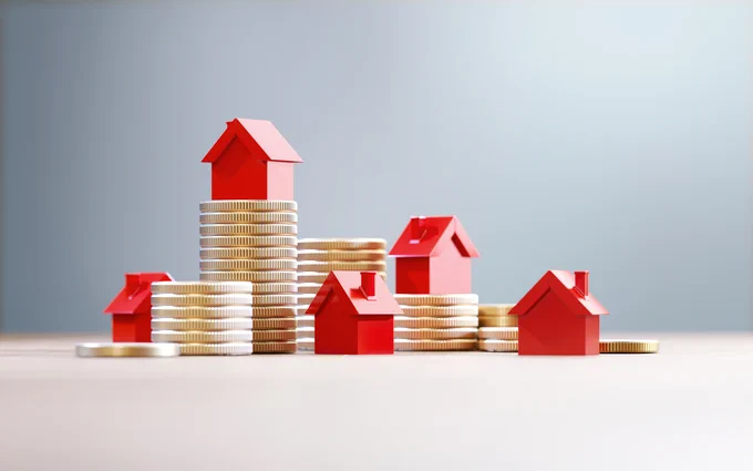 Stacks of gold coins topped with small red house models symbolizing real estate investment growth.