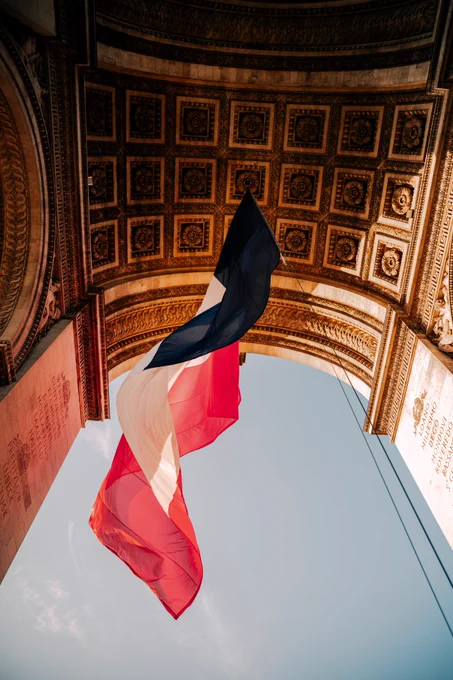 Photographie prise en contre-plongée sous l'Arc de Triomphe à Paris. On y voit le drapeau de la France.  