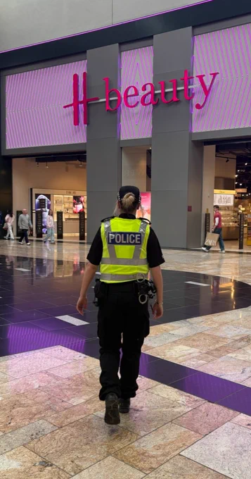 A police officer walks through a shopping mall in front of a large 'H beauty' store.