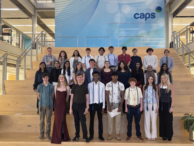 A large group of CAPS Bioscience posing together in CAPS atrium with CAPS branding visible.