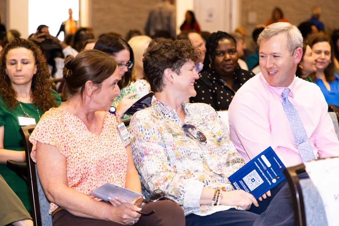 Faculty and staff smiling while sitting in rows.