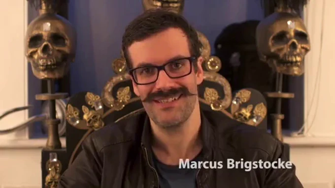 Comedian Marcus Brigstocke, sat upon a throne with skulls.