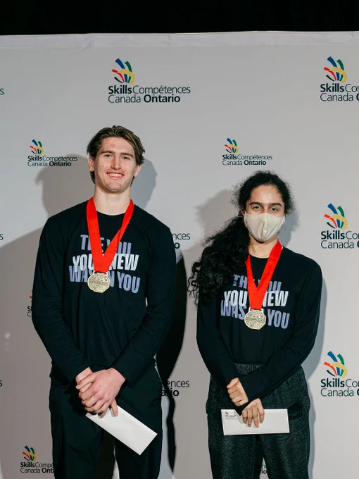 Two people stand together and both have medals around their necks.
