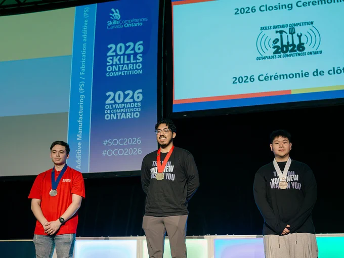 Three people stand on a stage with medals around their necks.
