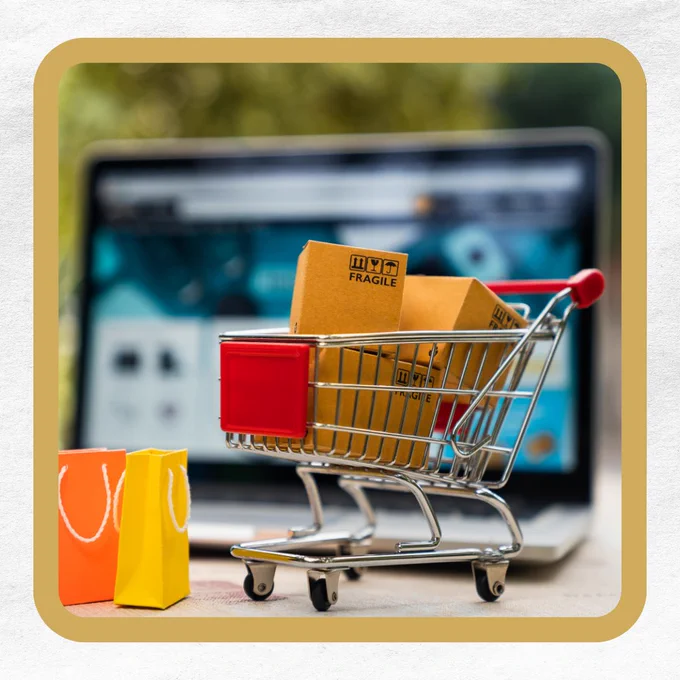 A miniature shopping cart with boxes labeled "FRAGILE" in front of a blurred computer screen.