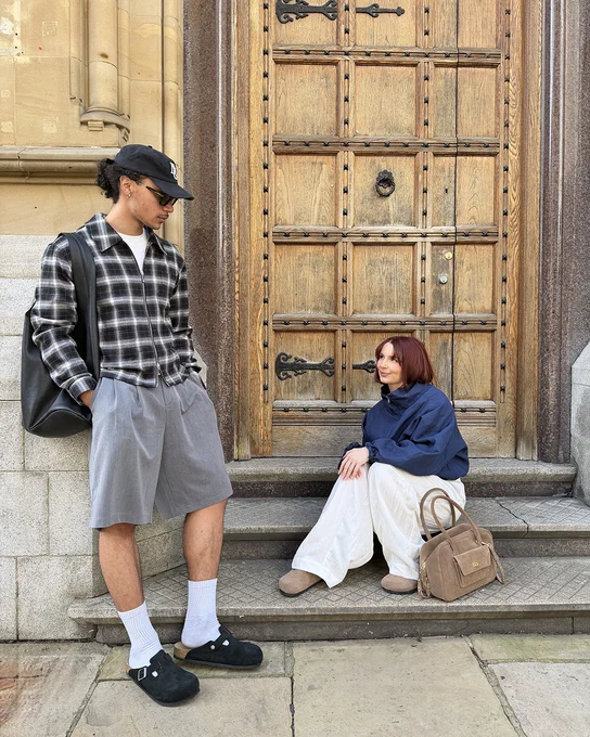 An image of two people wearing pairs of BIRKENSTOCK Boston Clogs whilst sitting and standing in front of a wooden doorway.