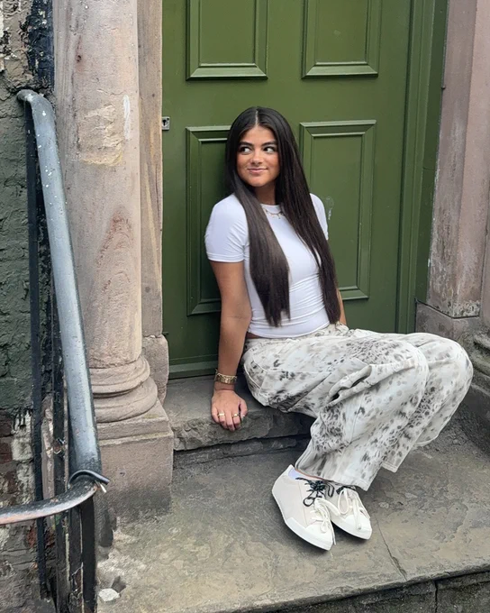 An image of a person wearing a pair of off white Converse Chuck Taylor Lo trainers whilst sitting against a green door.