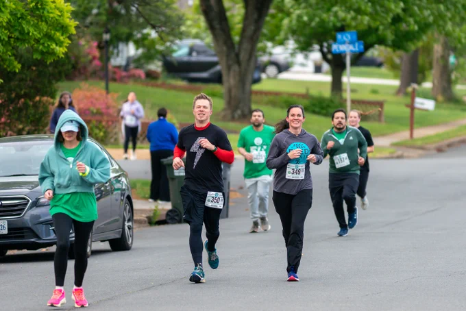 A lively scene of multiple runners participating in a community race along a residential street. The mood is energetic and the participants appear focused and determined.
