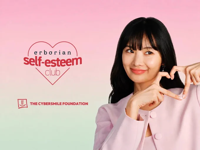 A girl making a heart with her fingers with Cybersmile and Erborian logos on a gradiant background.