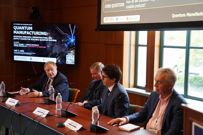 Patrick McCluskey speaks to his three other panel members with a screen reading "Quantum Manufacturing" behind him