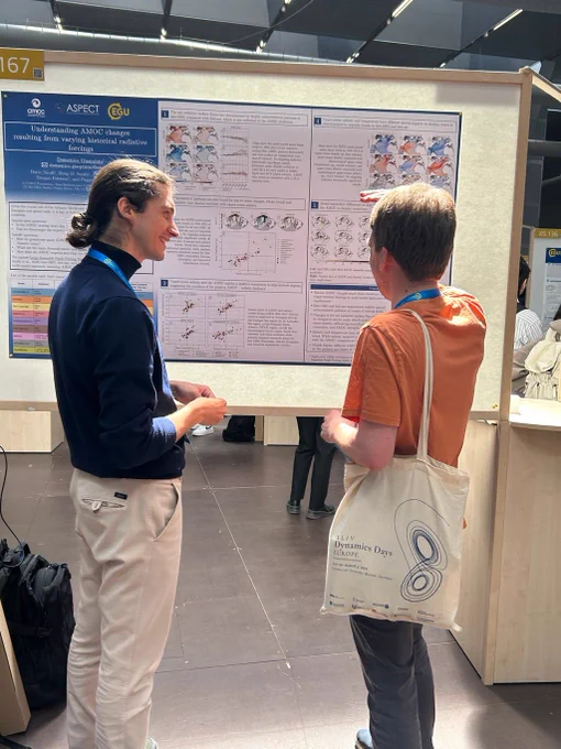 Two conference attendees stand side-by-side discussing a scientific poster on AMOC changes, pointing at charts and maps on a display board.