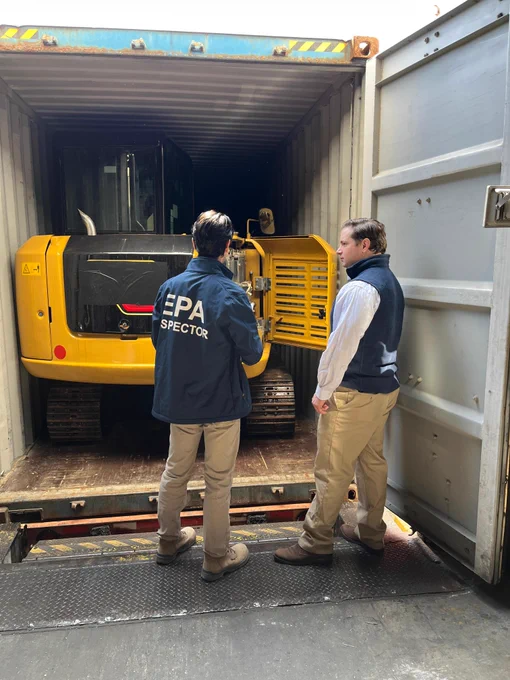 EPA inspector demonstrating a Clean Air Act import inspection of a diesel excavator in a shipping container, to verify if the excavator is certified with EPA, along with EPA senior leader.