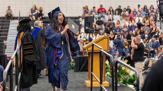 Wake Tech graduate walking across the stage smiling with her diploma in hand.