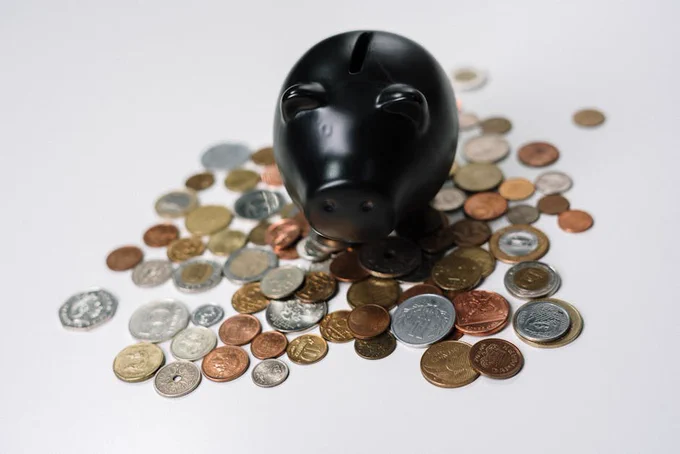 Black piggy bank surrounded by a variety of coins on a white surface.