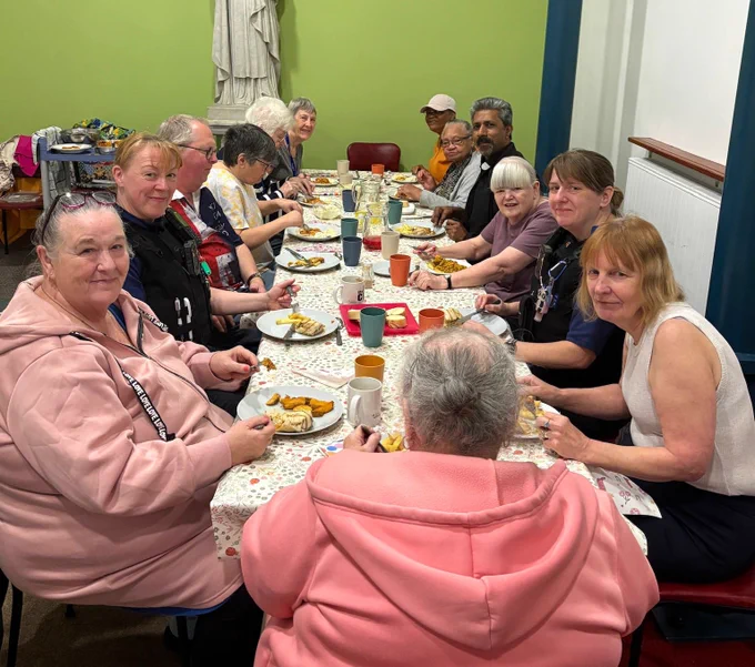 Group of people sharing a meal around a long table in a room with green walls