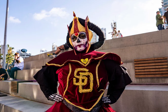 Photo of a Padres fan who is dressed up as Padmé Amidala for Star Wars Weekend. Her face is painted like a sugar skull. The dress she is wearing has gold SD logo and a gold PS heart.