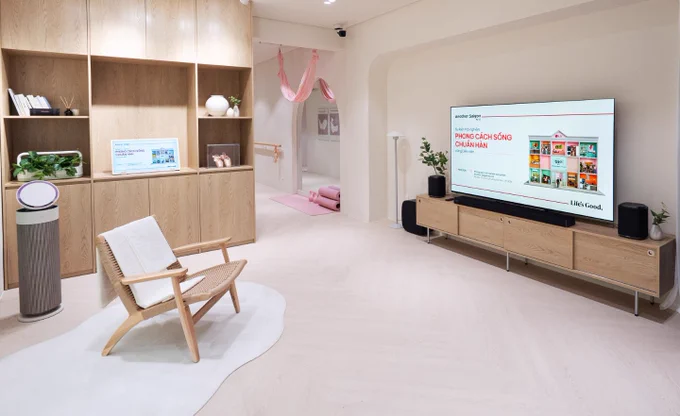 LG lifestyle experience space featuring a large LG TV displaying a Vietnamese presentation, an LG air purifier, a small screen on wooden shelving, speakers, plants, and a pastel wellness area in the background.
