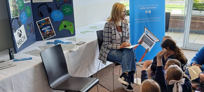 A woman sitting on a chair talking to a group of primary school children who are sitting on the floor in front of her.