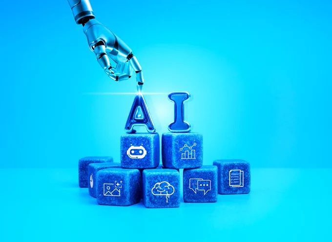Image has a blue background with blue building blocks with the letters AI at the top, with a digital hand putting the A into position.