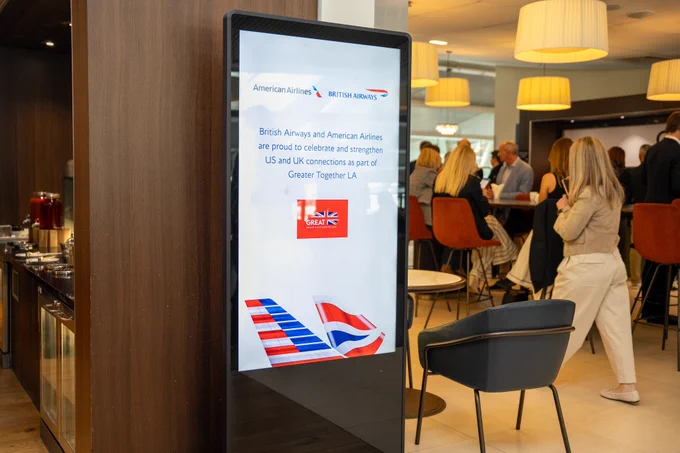 A digital sign in the airport lounge displays a sign that reads "British Airways and American Airlines are proud to celebrate and strengthen U.S. and UK connections as part of Greater Together LA".
