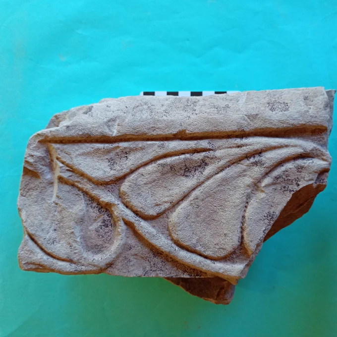 A piece of pale grey stone carved with a flowing foliage design.