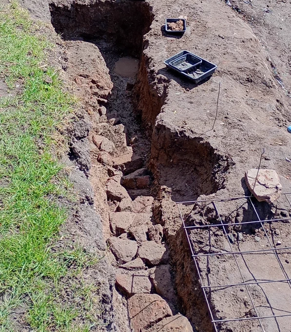 A drainage ditch lined with large fragments of stone, seen from above.
