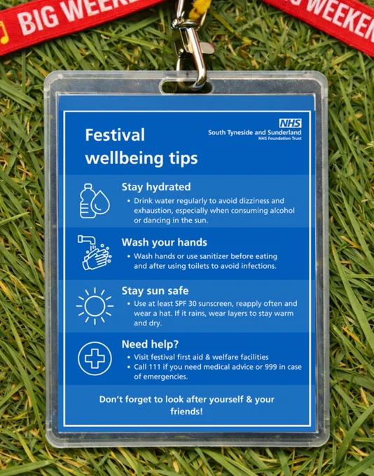 A festival lanyard with a badge displaying "Festival wellbeing tips" on grass. The badge includes advice to stay hydrated, wash hands, stay sun safe, and where to find medical help. It features the NHS South Tyneside and Sunderland logo. The lanyard is red with "BIG WEEKEND" text in white.
