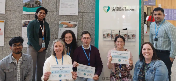 A team of people facing the camera in front of a poster, three of them are holding posters to support the TSC initiative