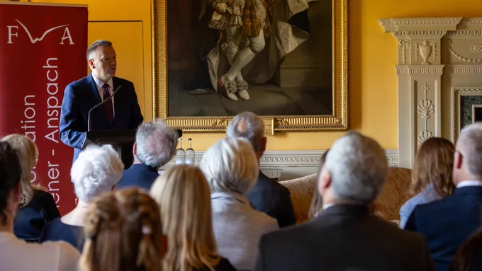 Minister for EU Relations, the Rt Hon Nick Thomas-Symonds MP, speaking at a podium in front of an audience. Behind the speaker, there is a large, framed painting on the wall. The room is elegantly decorated.