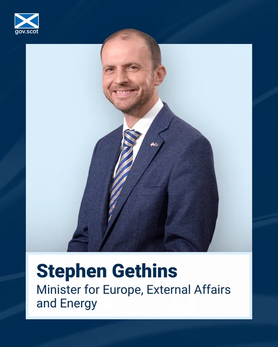 Porträtfoto einer Person im blauen Anzug mit gestreifter Krawatte vor hellem Hintergrund. Oben links ist das gov.scot-Logo zu sehen. Unten im Bild steht: „Stephen Gethins – Minister for Europe, External Affairs and Energy“.