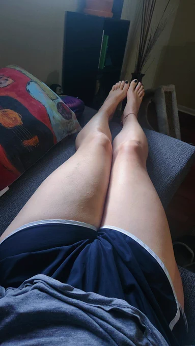 a photo of my thighs and legs outstretched on a couch from my POV. there is a pillow next to them
