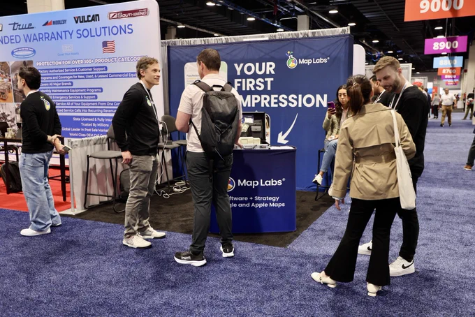 People interacting at a trade show booth featuring a banner for Map Labs. The mood is professional and engaging.