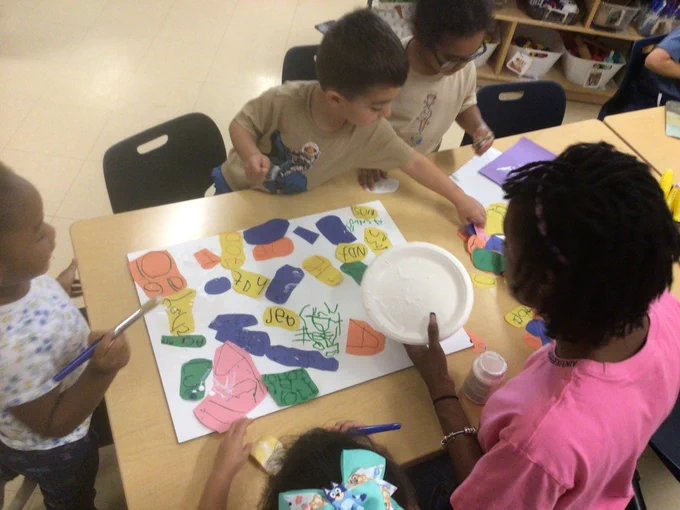 Children and a volunteer artist working on their artwork together.