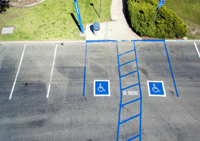 Accessible parking spaces with blue wheelchair symbols and striped no-parking access aisle beside a sidewalk entrance.