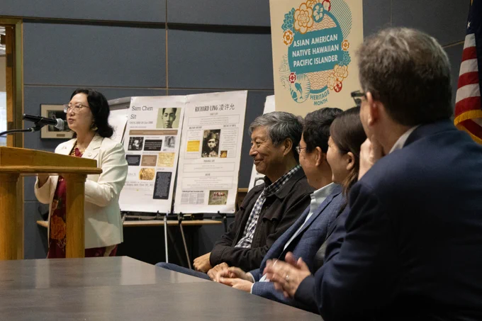 AANHPI panelists listen to Director Anna Hui deliver a speech at a podium.