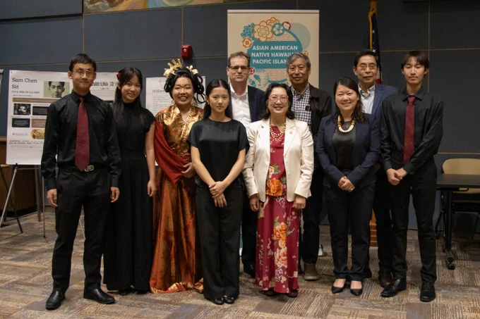 Group of nine participants and Director Anna Hui dressed formally and in traditional attire posing indoors at an Asian American Native Hawaiian Pacific Islander event.