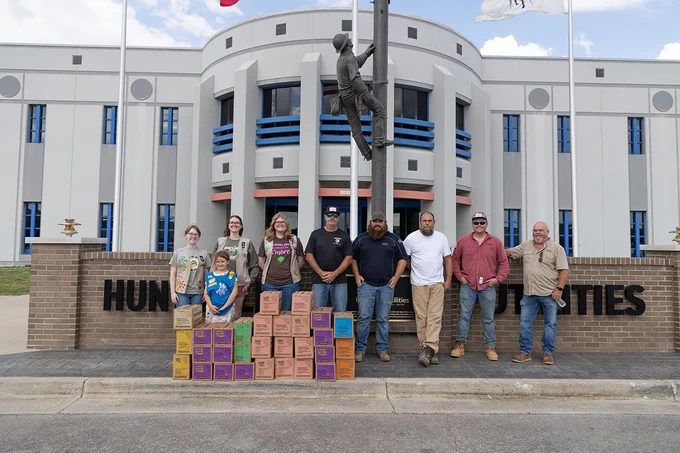 Group of Girl Scouts with cases of cookies and a group of electric lineworkers. 